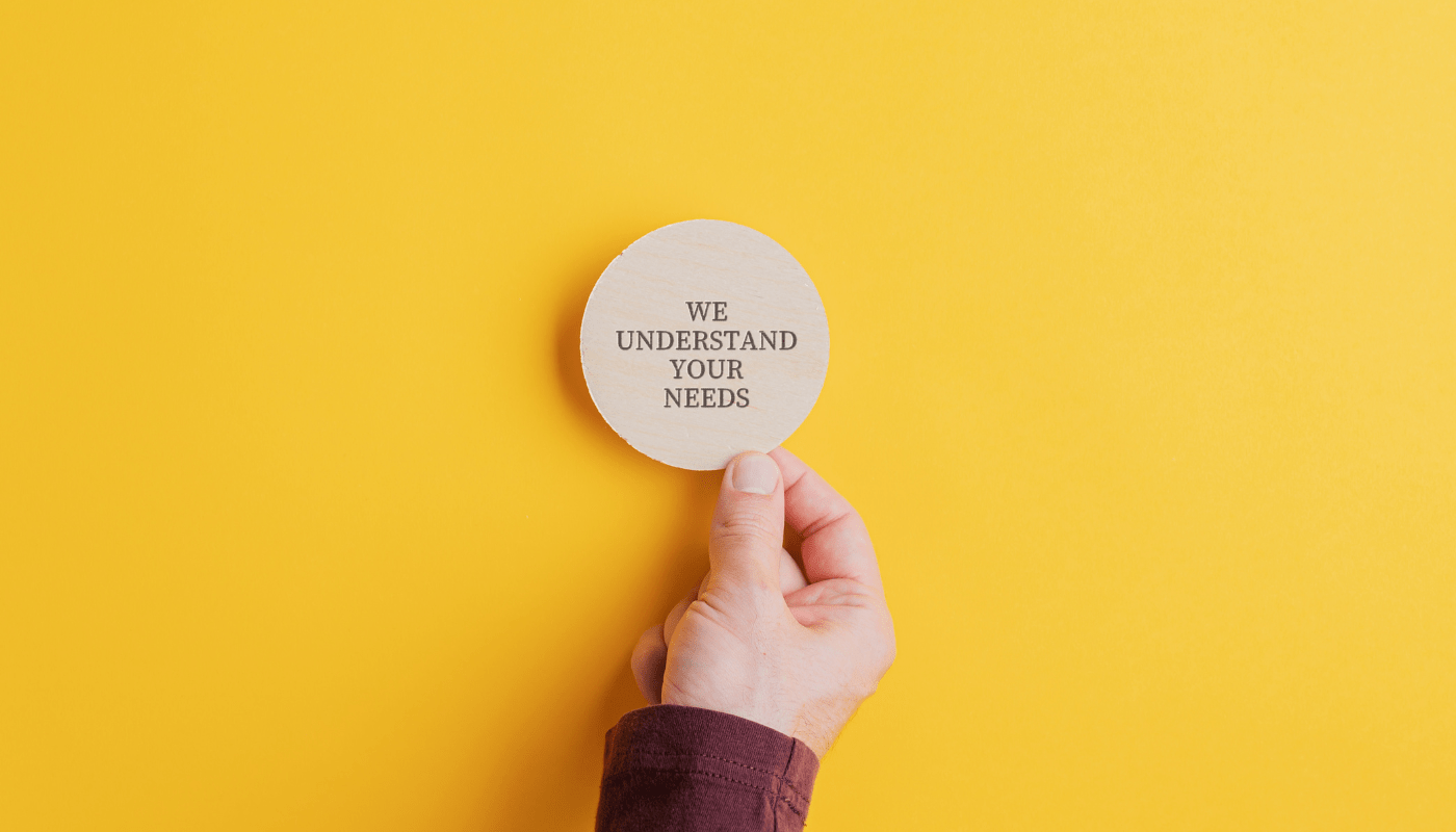 A hand holding up a wooden plate with the text "We understand your needs" in front of a yellow background.